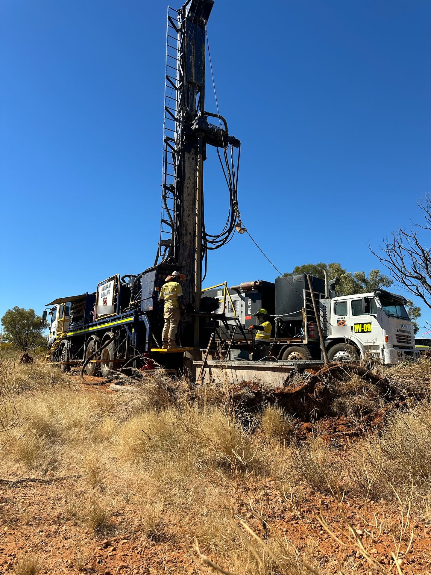 Truck-mounted rig drilling in dry spinifex country with a support truck alongside