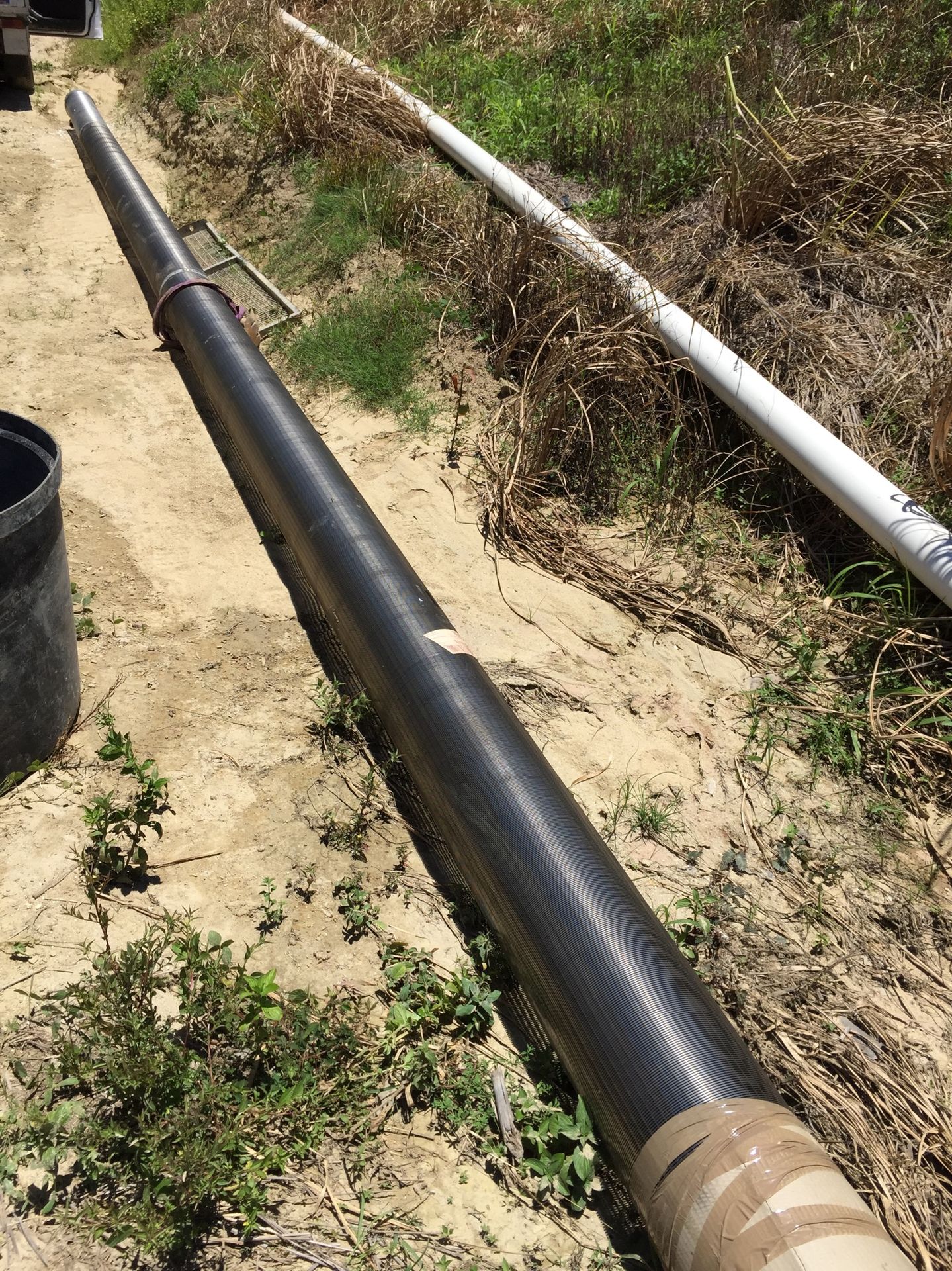 Length of slotted bore screen laid out on sandy ground beside the site